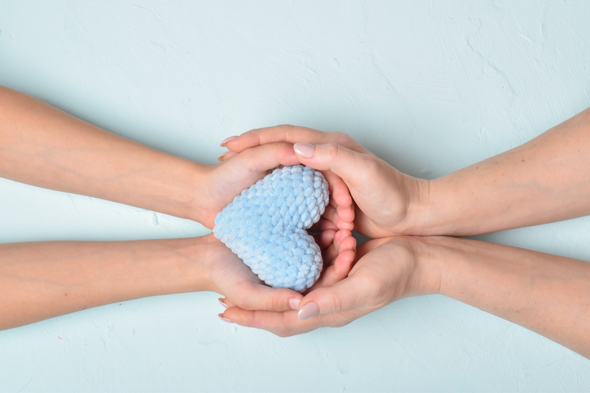 The baby passes the blue knitted heart into his mother's hands. Softness